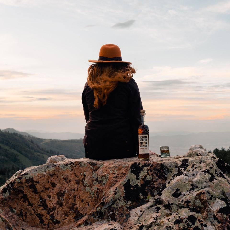 Person sitting on a rock with a bottle, looking at a scenic landscape